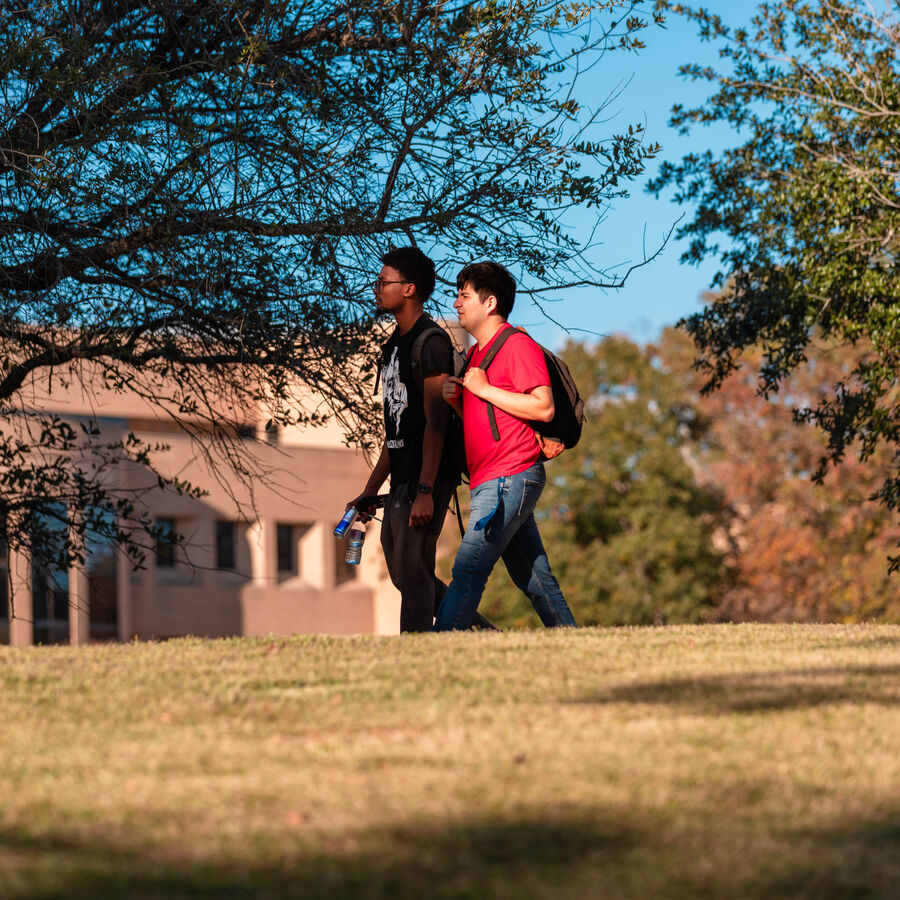 Two male students walk outdoors through the UT Tyler campus