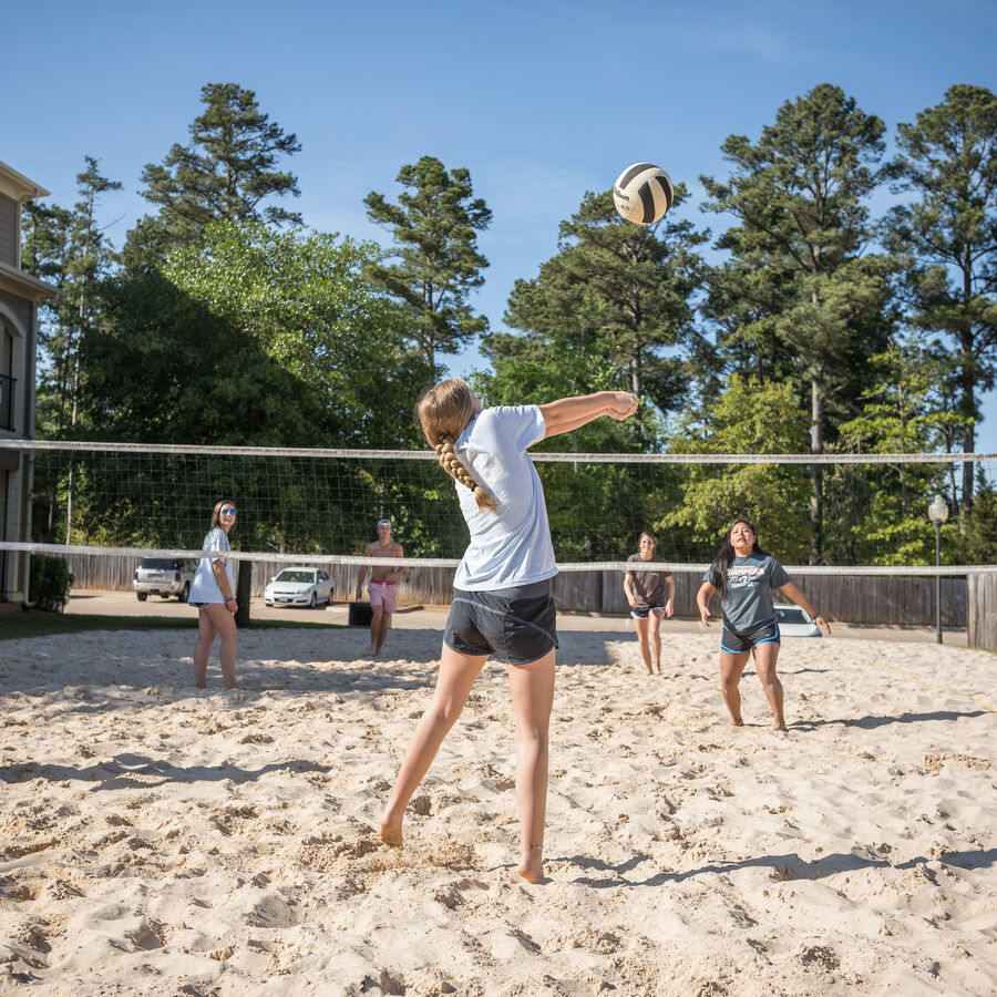 A group of male and female students play volleyball in the sand outside of the Liberty Landing Apartments at The University of Texas at Tyler