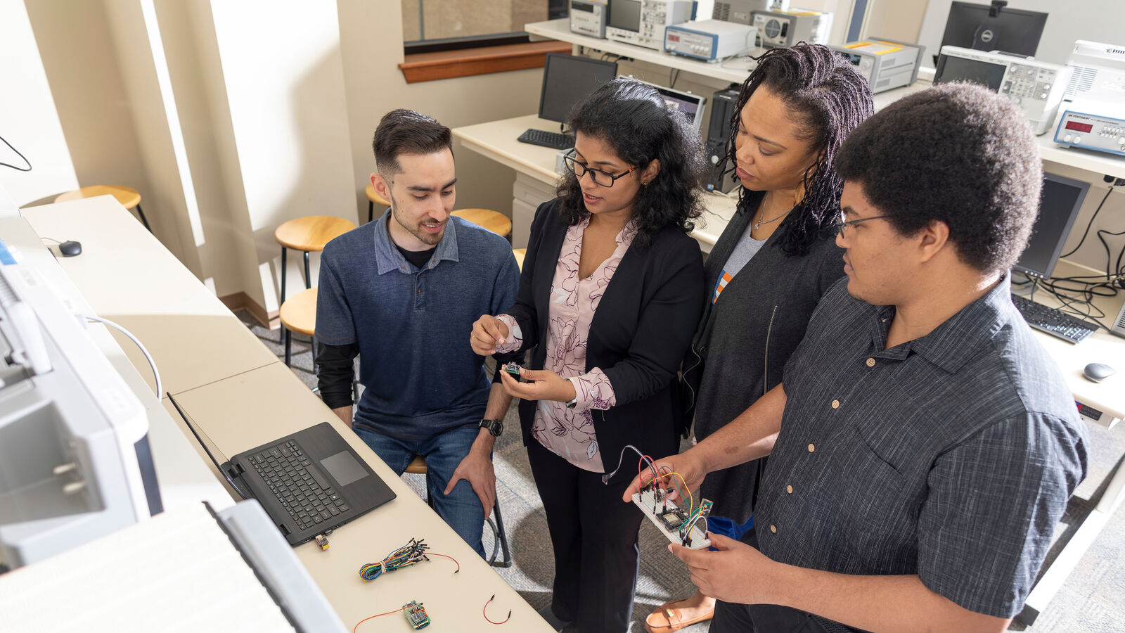 Professor and computer engineering students interact on an electric engineering project