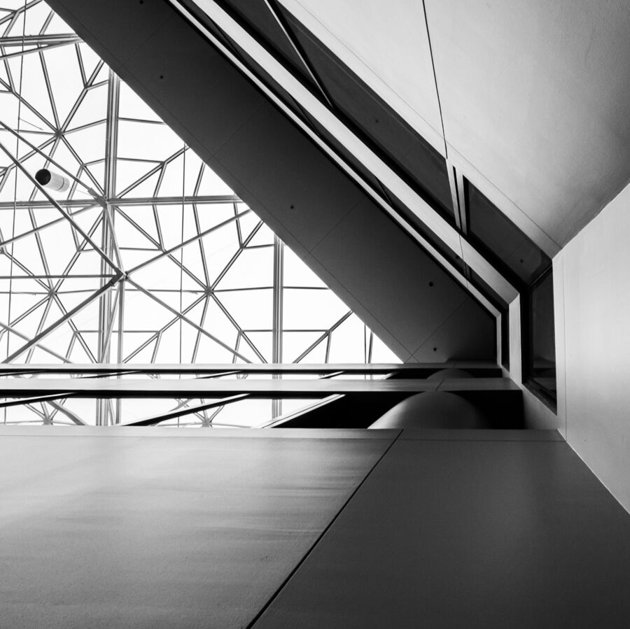 A black and white image of architectural details of the Houston Engineering Center. The camera is pointed upward at the glass ceiling while the photographer stands at the point where three walls connect.