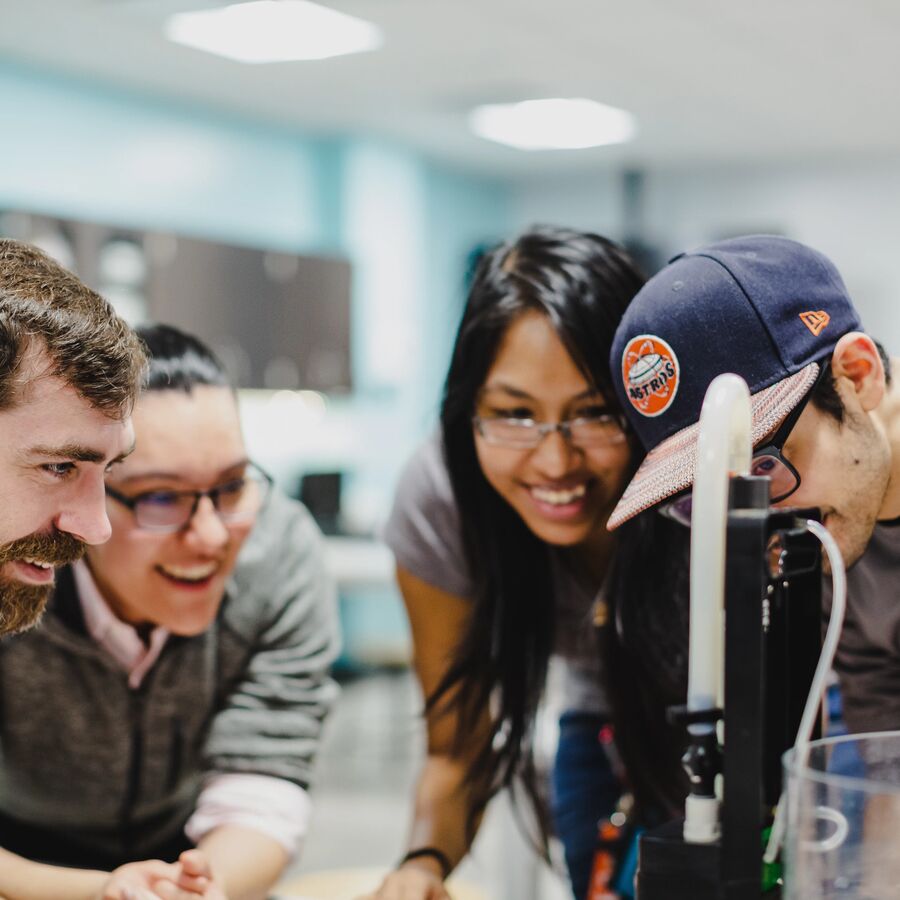 Several smiling students gather around their project in a classroom at UT Tyler's Houston Engineering Center
