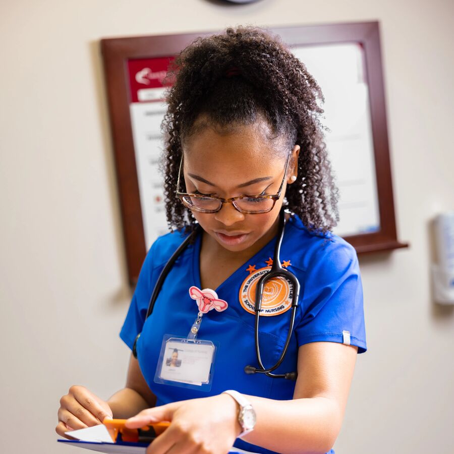A female School of Nursing student wearing scrubs examines information on a clipboard