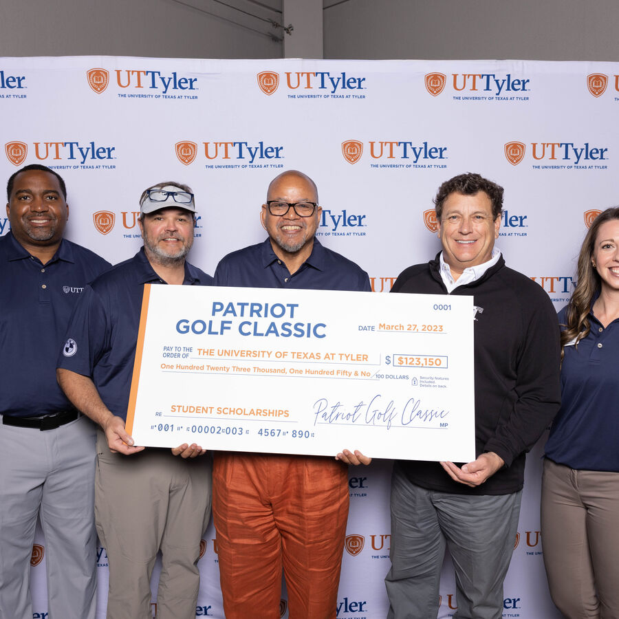 University of Texas at Tyler alumni hold a large check at a fundraising event