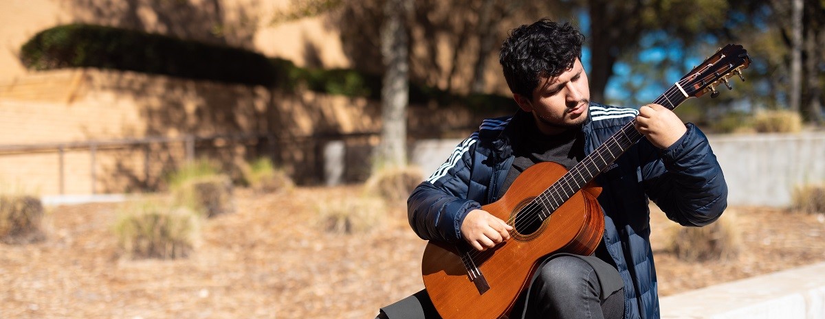 Student playing an acoustic guitar outside the CMA