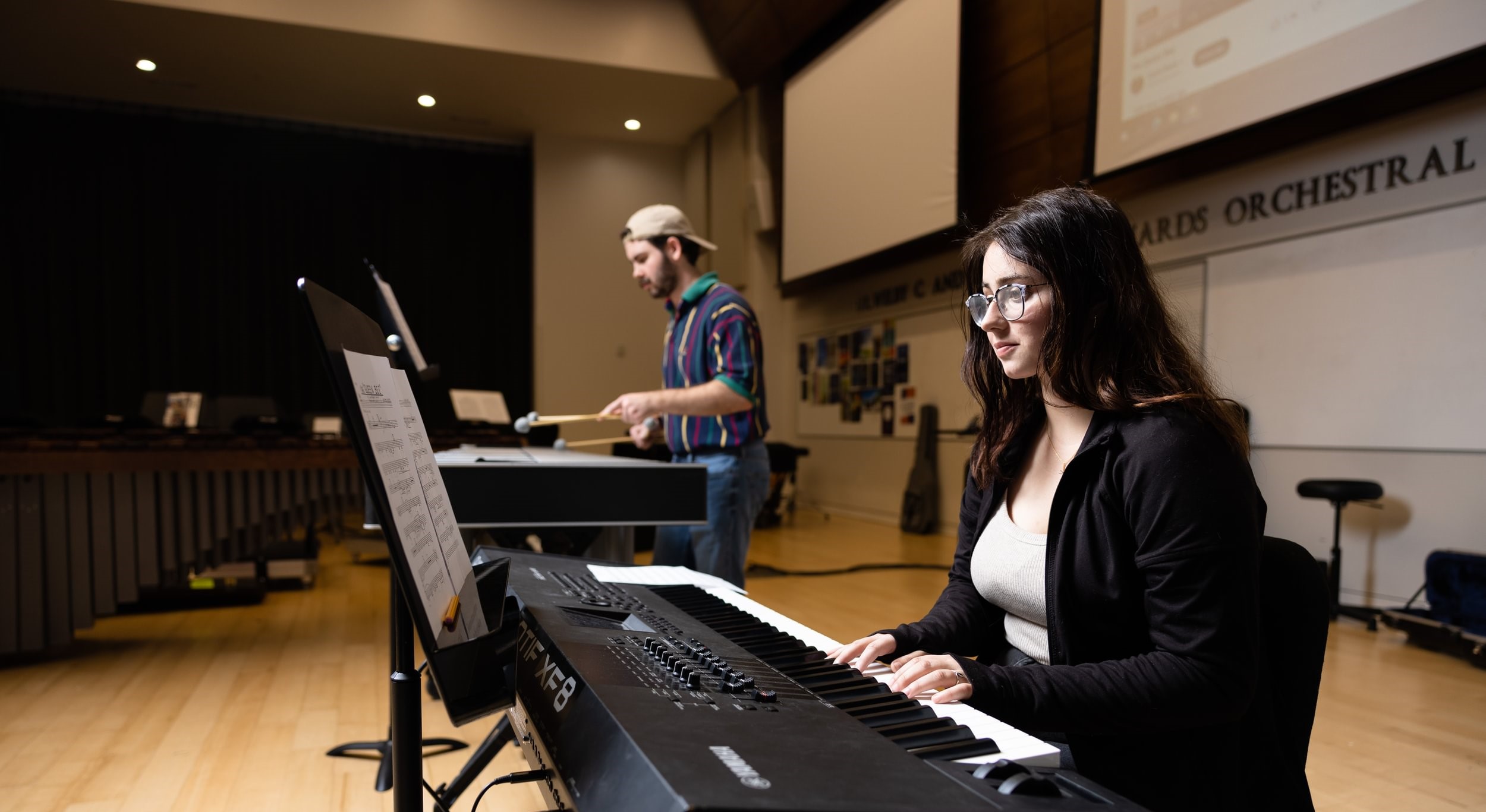 Music student playing on a keyboard with a student playing the marimba