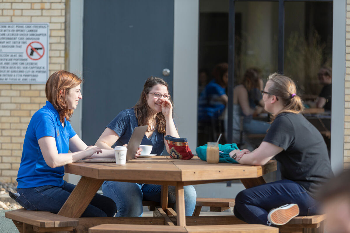 A student with two friends at a cafe, talking while working on school.