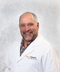 man in white coat,smiling. man is bald with facial hair.