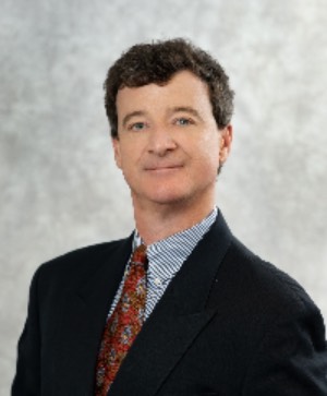 man with dark hair, wearing a black suit jacket and red, patterned tie. 