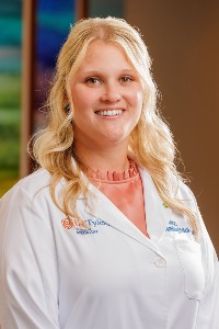 image of woman with long, blonde hair and blue eyes smilling, in a white coat and pink blouse.