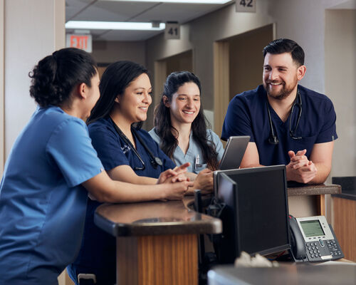 residents gathered around a nurses station reviewing a chart together