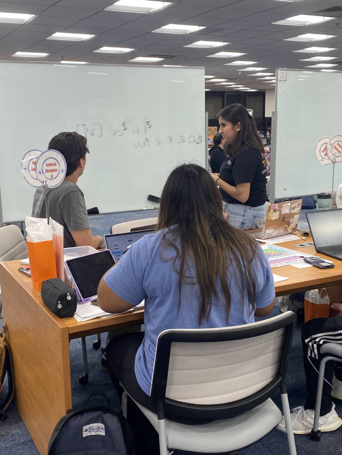 A Supplemental Instruction Leader breaks down chemistry concepts on a whiteboard while students collaborate and take notes.