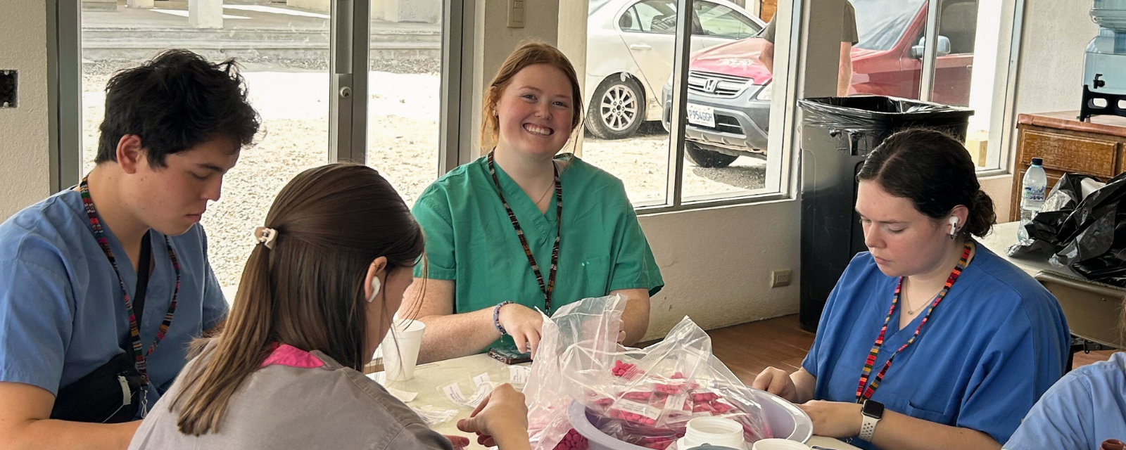 Nursing student wearing scrubs sits at table in sorting medical equipment.