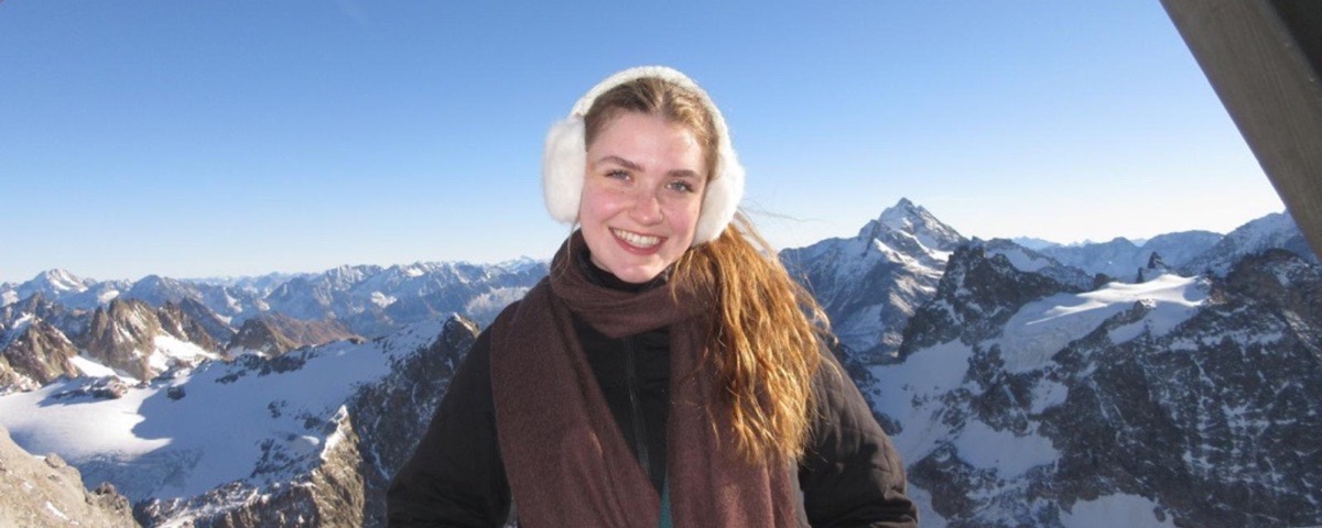 Student wearing earmuffs in front of a snowcapped mountainscape.