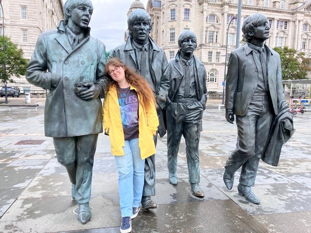 Girl in yellow jacket leaning against a statue of 4 guys